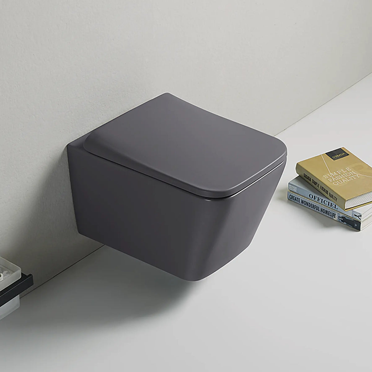 Gray wall-mounted toilet against a white wall with books on a shelf.